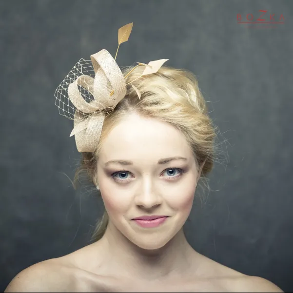 Beżowy fascynator na głowę z piórkami i woalką.