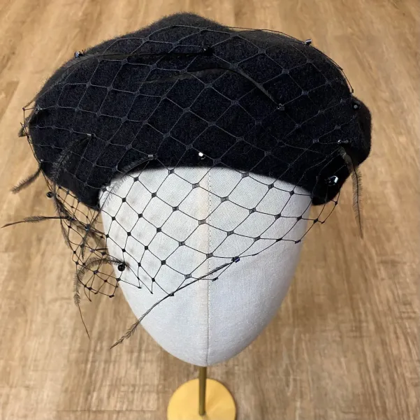 Czarny beret z woalką, piórkami i kryształkami.