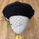 Czarny beret z woalką, piórkami i kryształkami.
