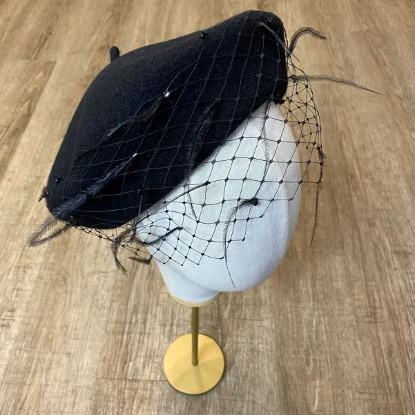 Czarny beret z woalką, piórkami i kryształkami.