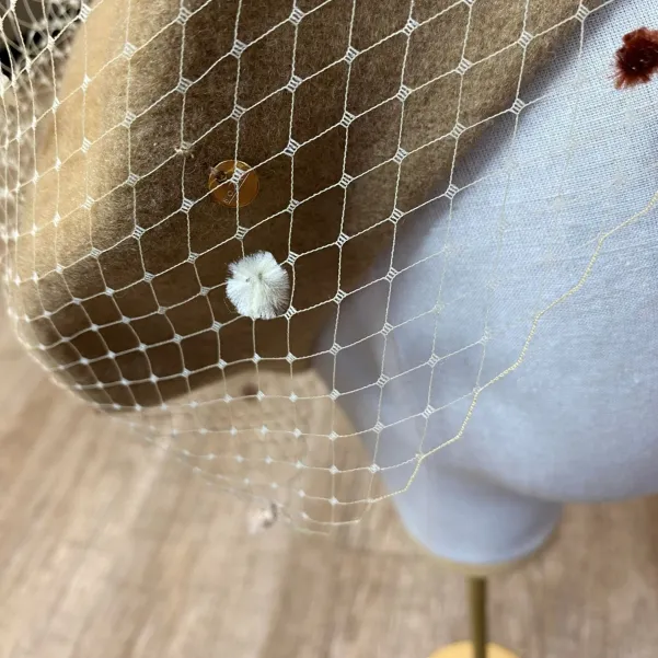 Beżowy beret z nakrapianą woalką.