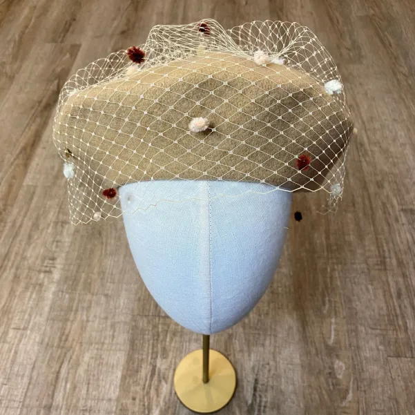 Beżowy beret z nakrapianą woalką.