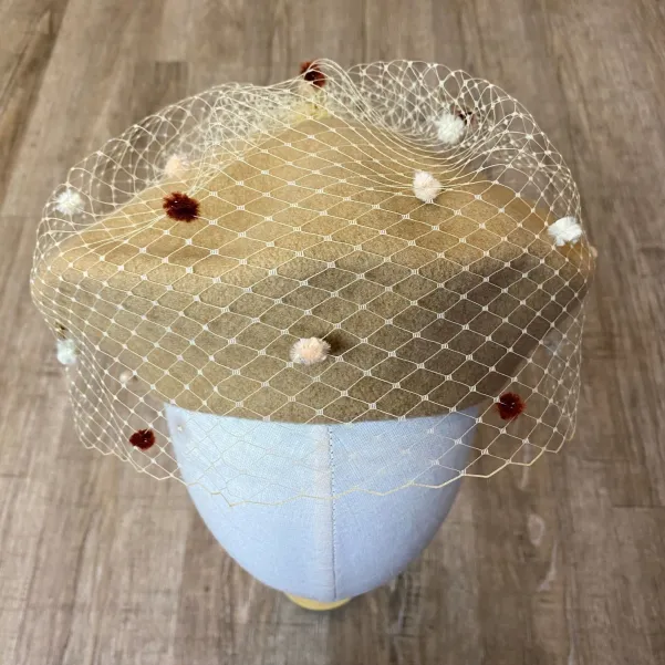 Beżowy beret z nakrapianą woalką.