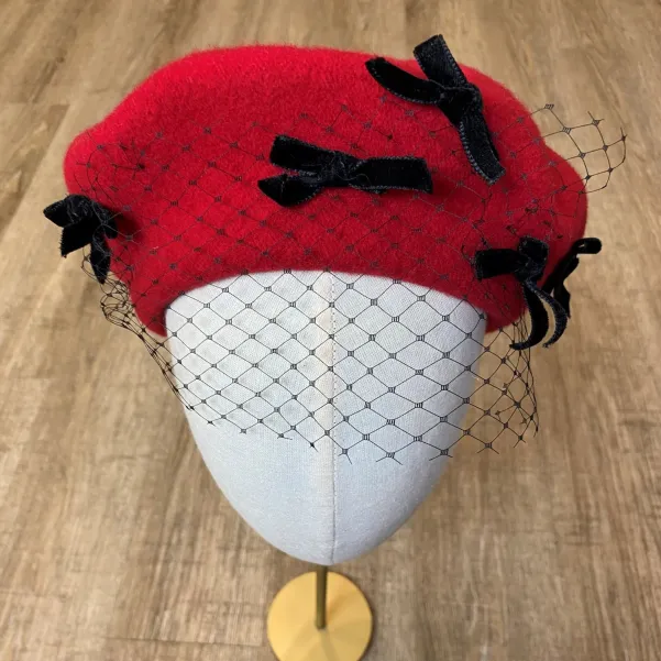Czerwony beret ozdobny z  kokardkami i z woalką.