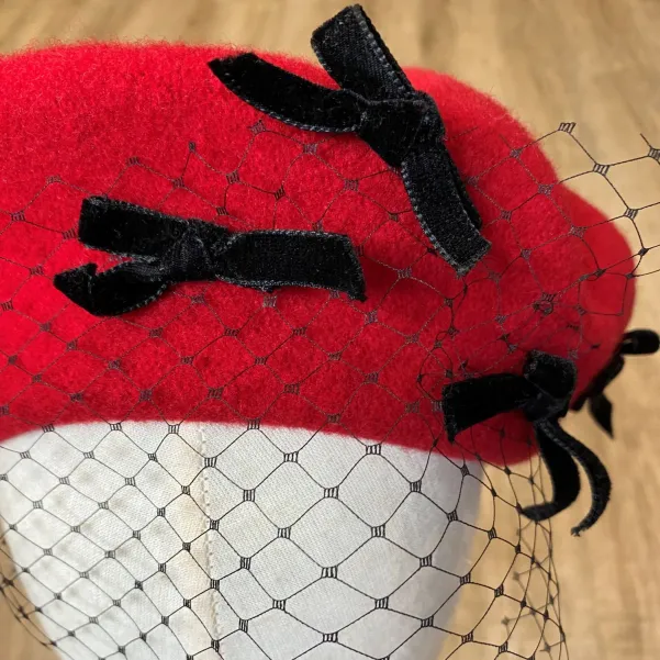 Czerwony beret ozdobny z  kokardkami i z woalką.