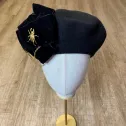 Stylowy beret z kokardą, łańcuchami i złotą ozdobą.